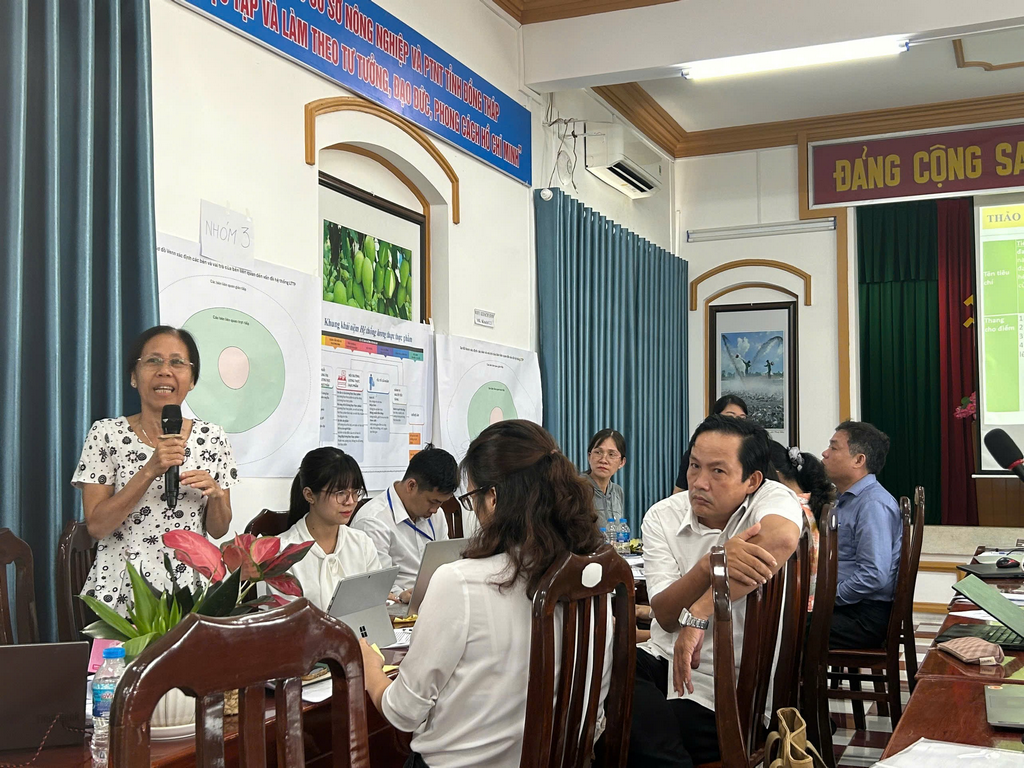 A person speaking into a microphone in front of a group of peopleDescription automatically generated